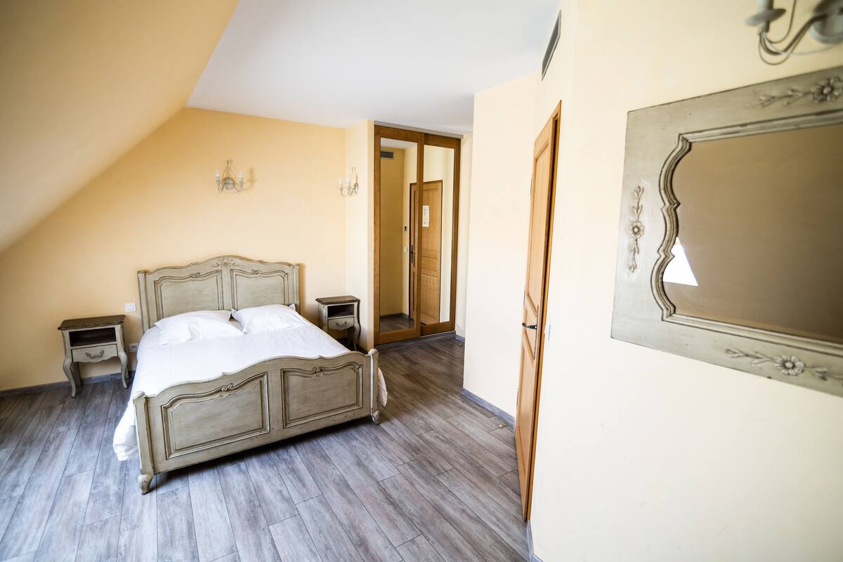 Un dormitorio con una cama grande, mesitas de noche de madera, un espejo y una puerta que da a otra habitación.