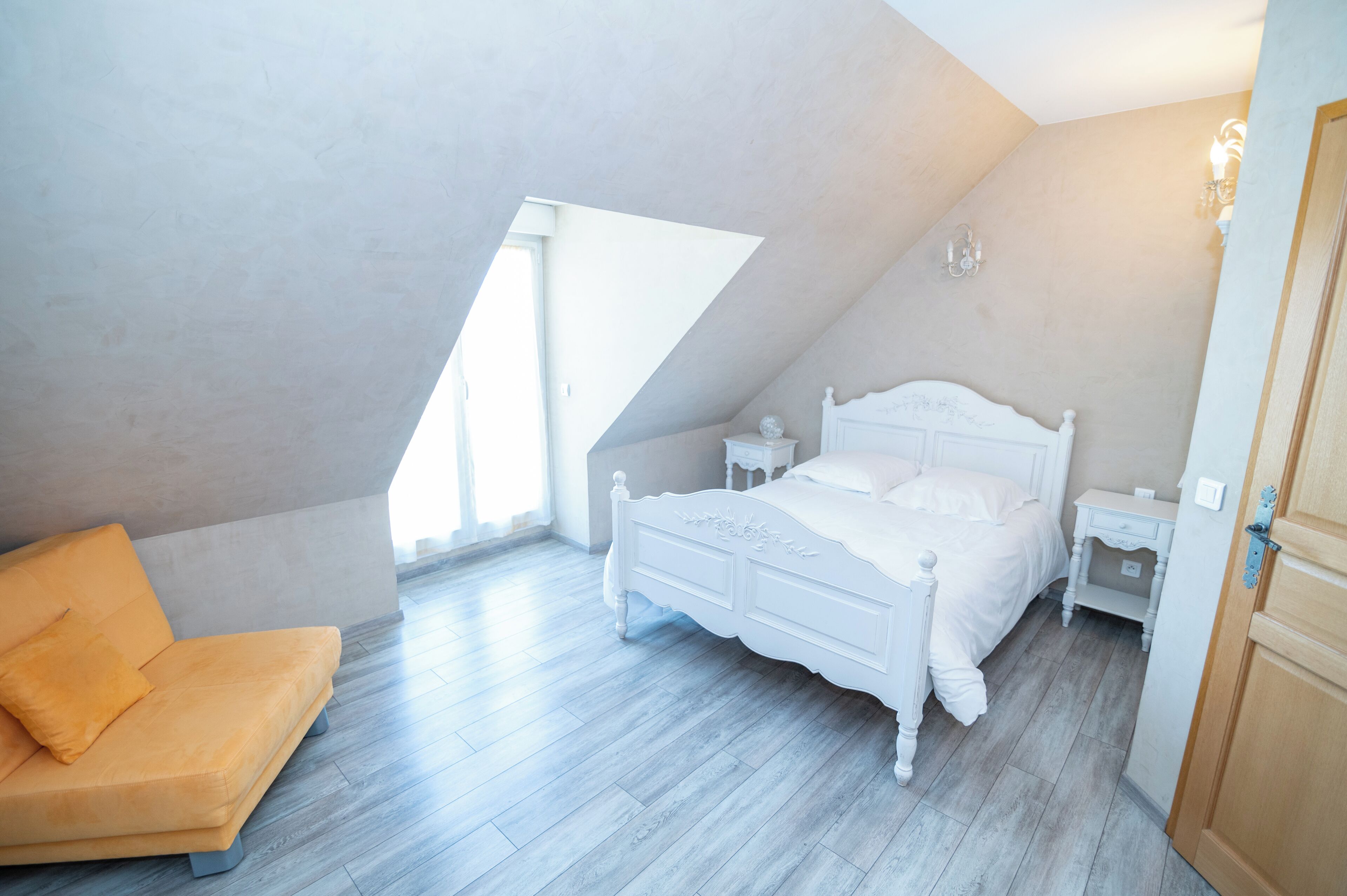 A bedroom with a sloped ceiling, a bed, a nightstand, a chair, and a wooden door.