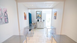 A hotel room with a kitchenette, a dining area with metal tables, and artwork on the walls.