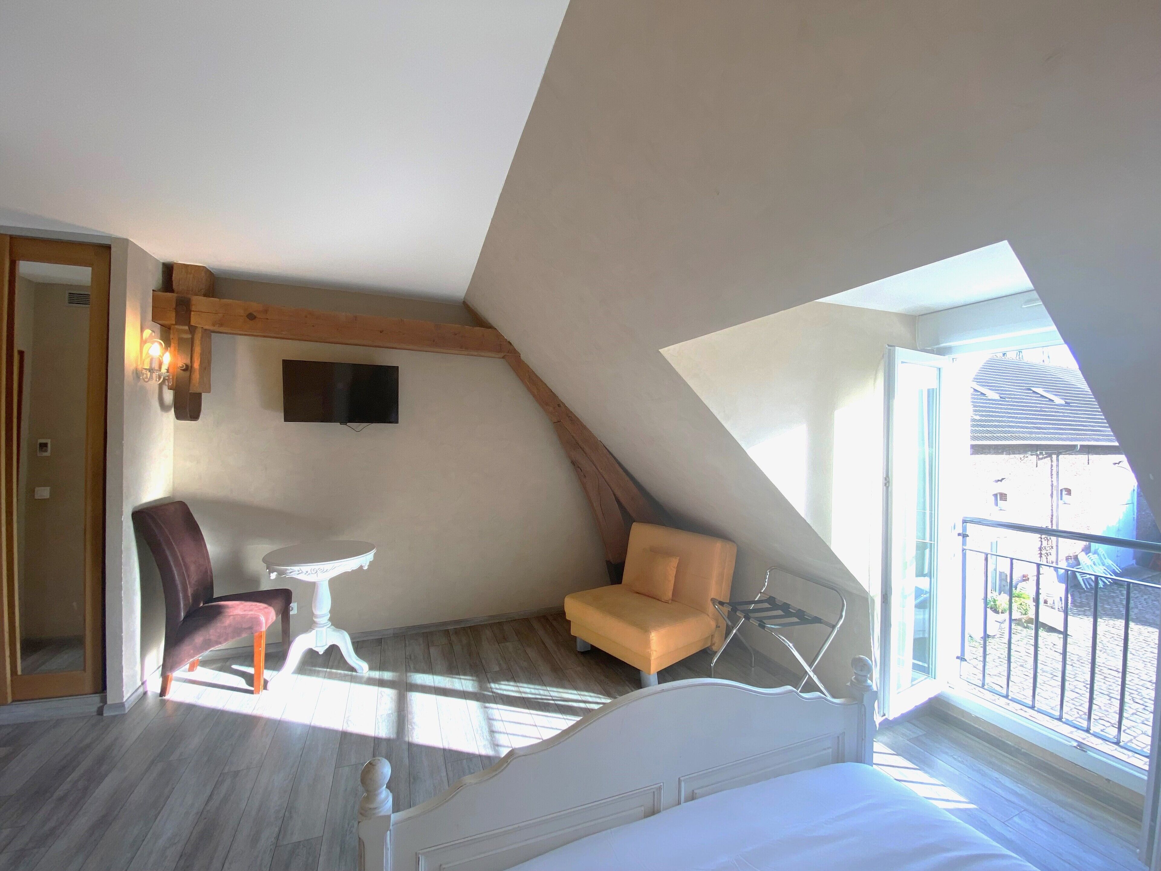 A bedroom with a sloped ceiling, a bed, a chair, a small table, and a TV mounted on the wall.