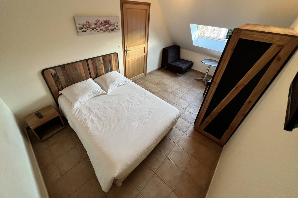 Un dormitorio con cama, una silla, una mesita, una puerta y una ventana.