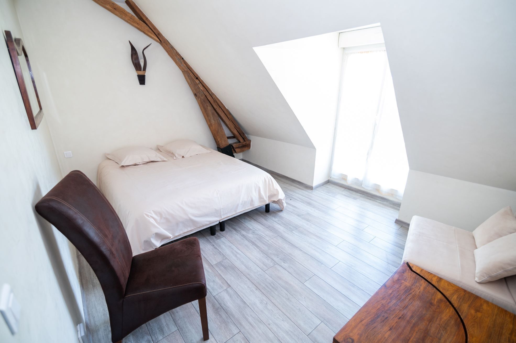 A bedroom with a sloped ceiling, a bed, a wooden chair, and a wooden table.