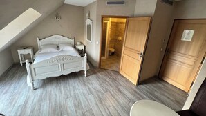 A bedroom with a sloped ceiling, a bed, bedside tables, a wardrobe, and a bathroom with a toilet and shower.