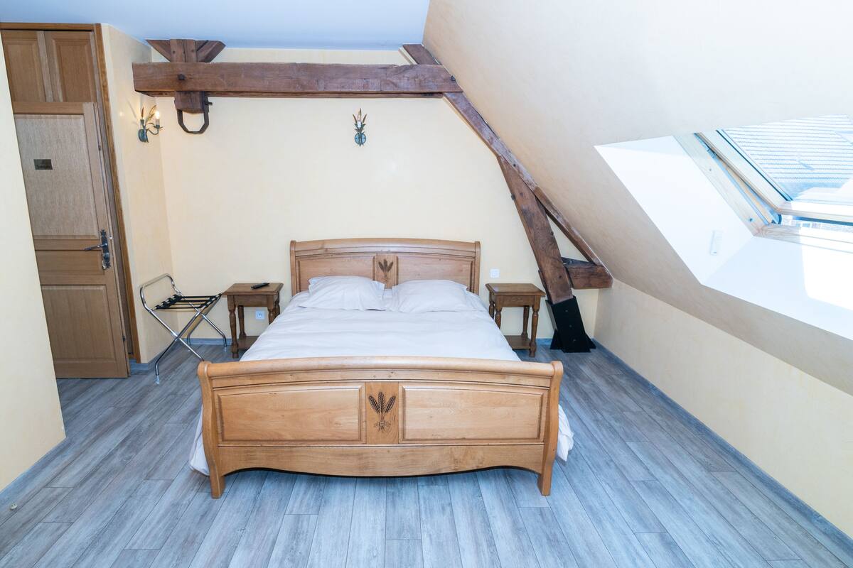 Un dormitorio con cama de madera, tragaluz, armario de madera y una mesita con lámpara.