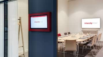 Un salón de conferencias con una gran mesa, sillas y una pantalla que muestra 'Intercity Hotel'.