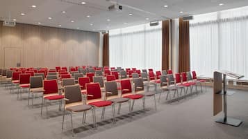 A conference room with rows of chairs, a podium, and large windows with curtains.