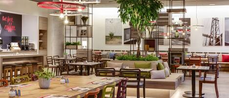 Un café moderno con mesas de madera, sillas coloridas y lámparas colgantes rojas.