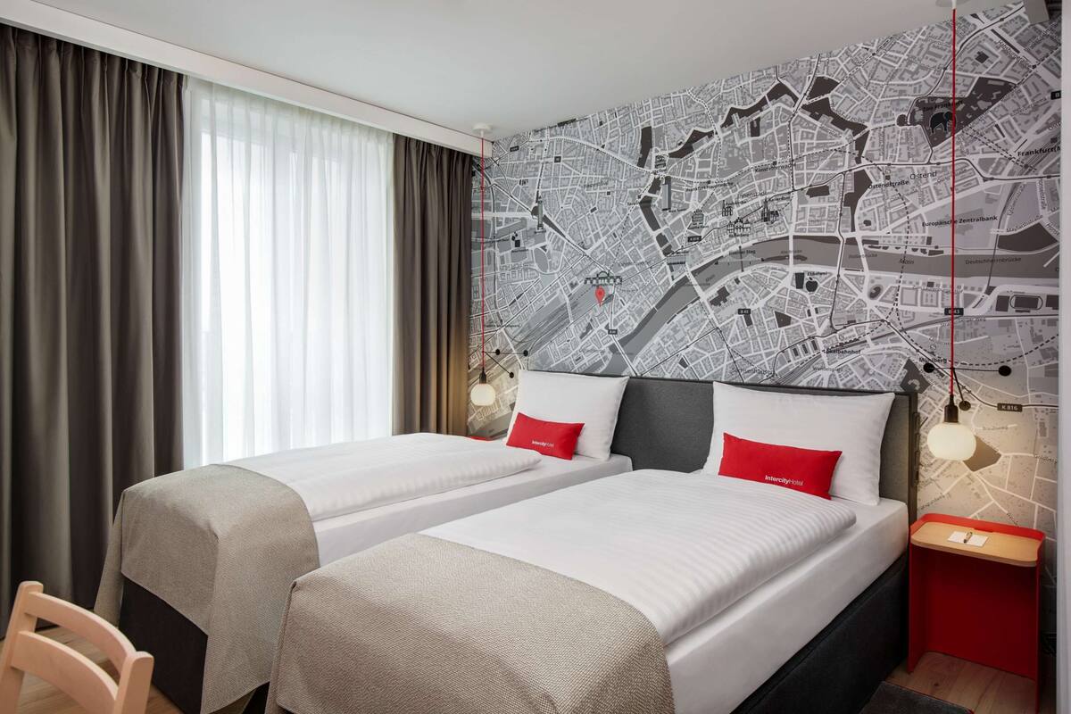 Une chambre d’hôtel avec deux lits, une carte de la ville accrochée au mur et une lampe rouge sur la table de chevet.