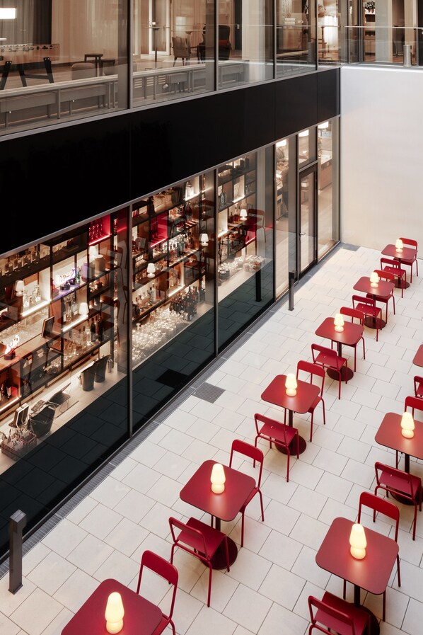 A modern indoor space with a glass facade, red chairs, and tables arranged in rows.