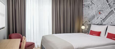 A hotel room with a bed, a desk, a chair, and a map on the wall.