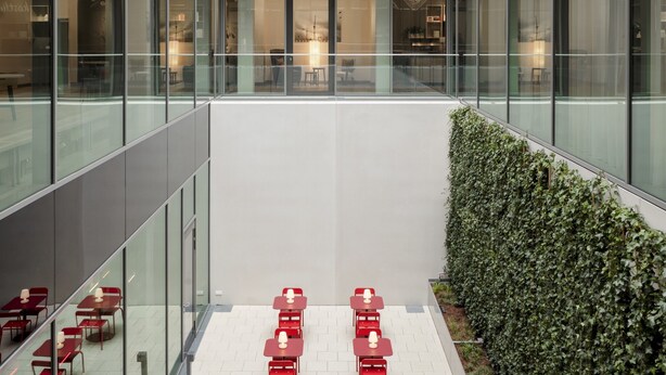 A modern building with a glass facade, a central courtyard with red tables and chairs, and a hedge along one side. - IntercityHotel Frankfurt Hauptbahnhof Süd (Frankfurt)