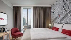 A hotel room with a large bed, a desk with a chair, a city view, and a map on the wall. - IntercityHotel Frankfurt Hauptbahnhof Süd (Frankfurt)