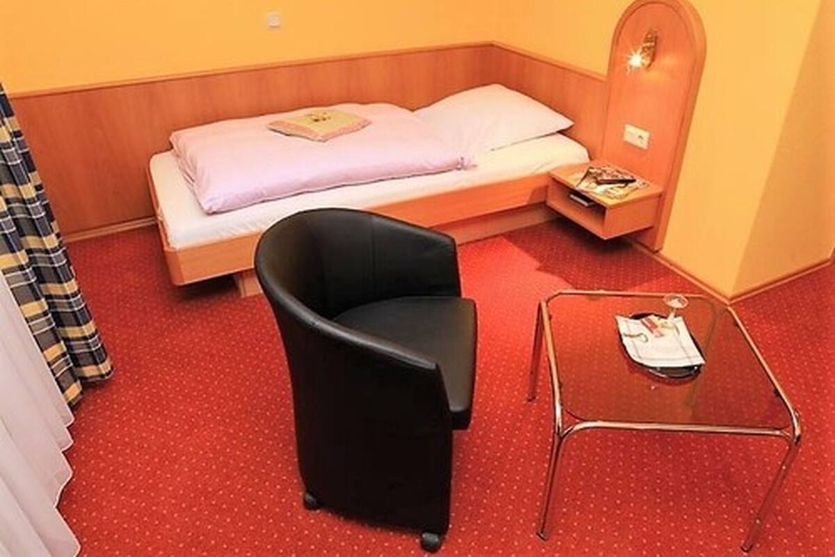 A small room with a single bed, a black chair, and a small table with a magazine.