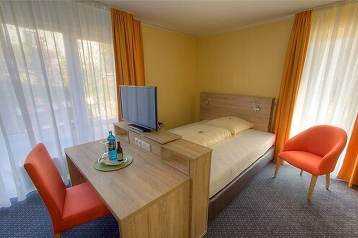 A hotel room with a bed, a desk with a chair, a television, and a bottle of water.