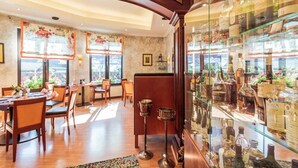 A restaurant with wooden tables and chairs, a glass display case with bottles, and large windows with curtains. - Hotel Restaurant Kasserolle (Siegburg)