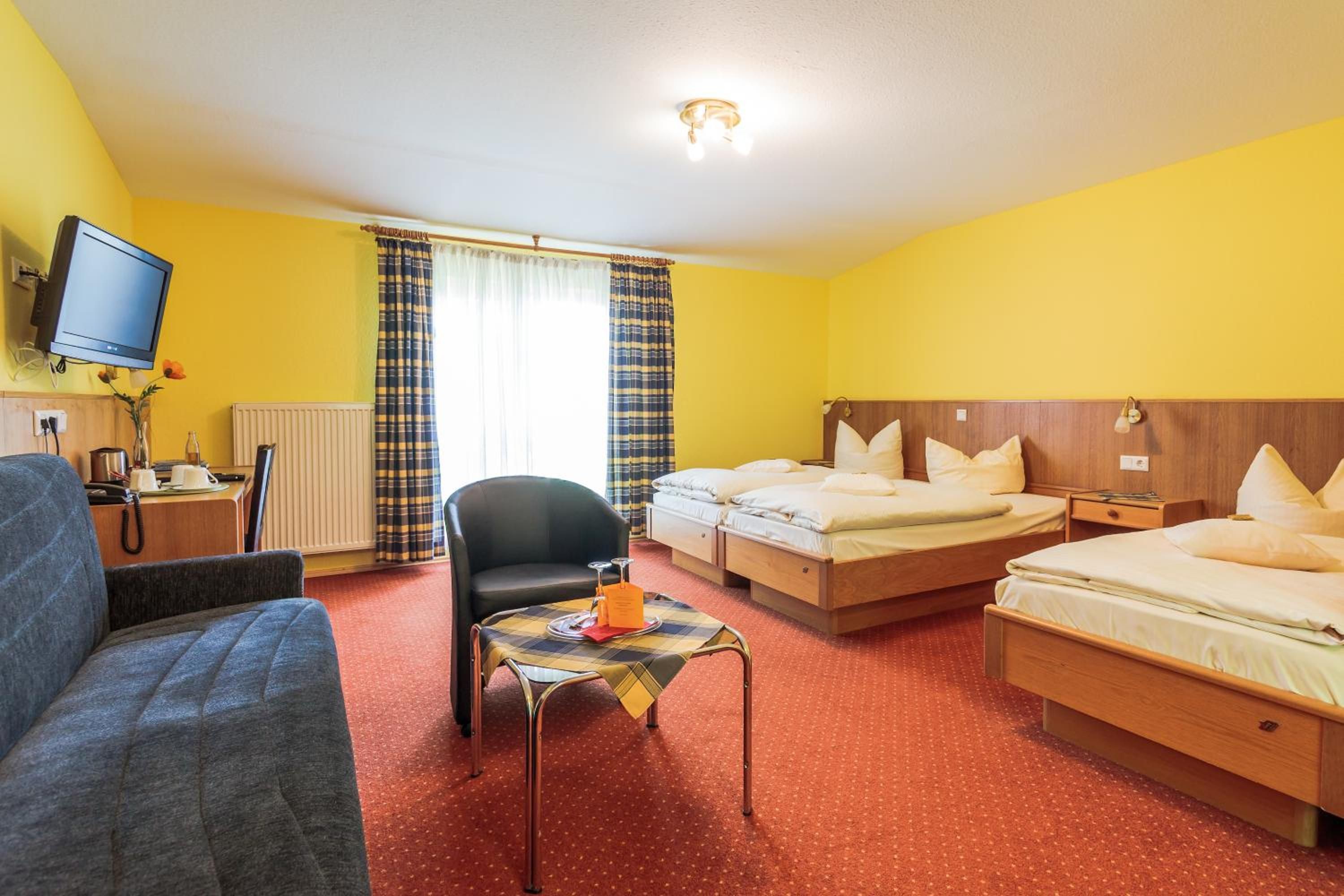 Ein Hotelzimmer mit einem Einzelbett, einer Couch, einem kleinen Tisch mit Tablett, einem Sessel, einem Fernseher und einem Fenster mit Vorhängen.