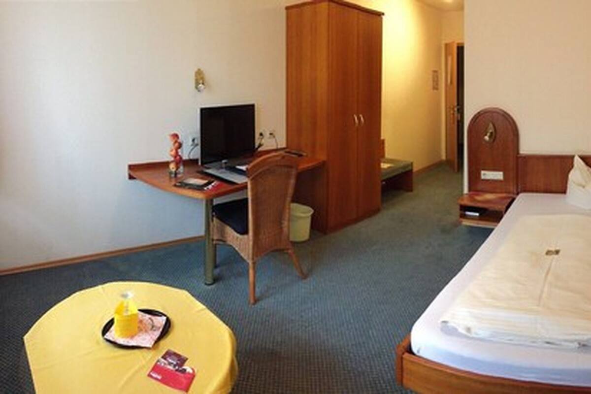 A hotel room with a bed, a desk with a computer, a chair, and a small table with a yellow tablecloth.