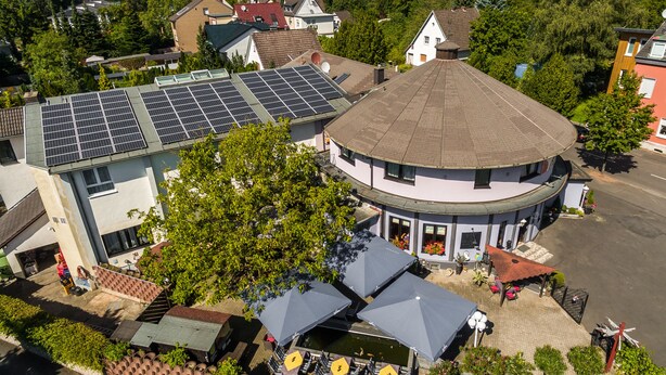A building with a round corner, a rooftop with solar panels, and outdoor seating with umbrellas. - Hotel Restaurant Kasserolle (Siegburg)