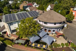 A building with a round corner, a rooftop with solar panels, and outdoor seating with umbrellas. - Hotel Restaurant Kasserolle (Siegburg)