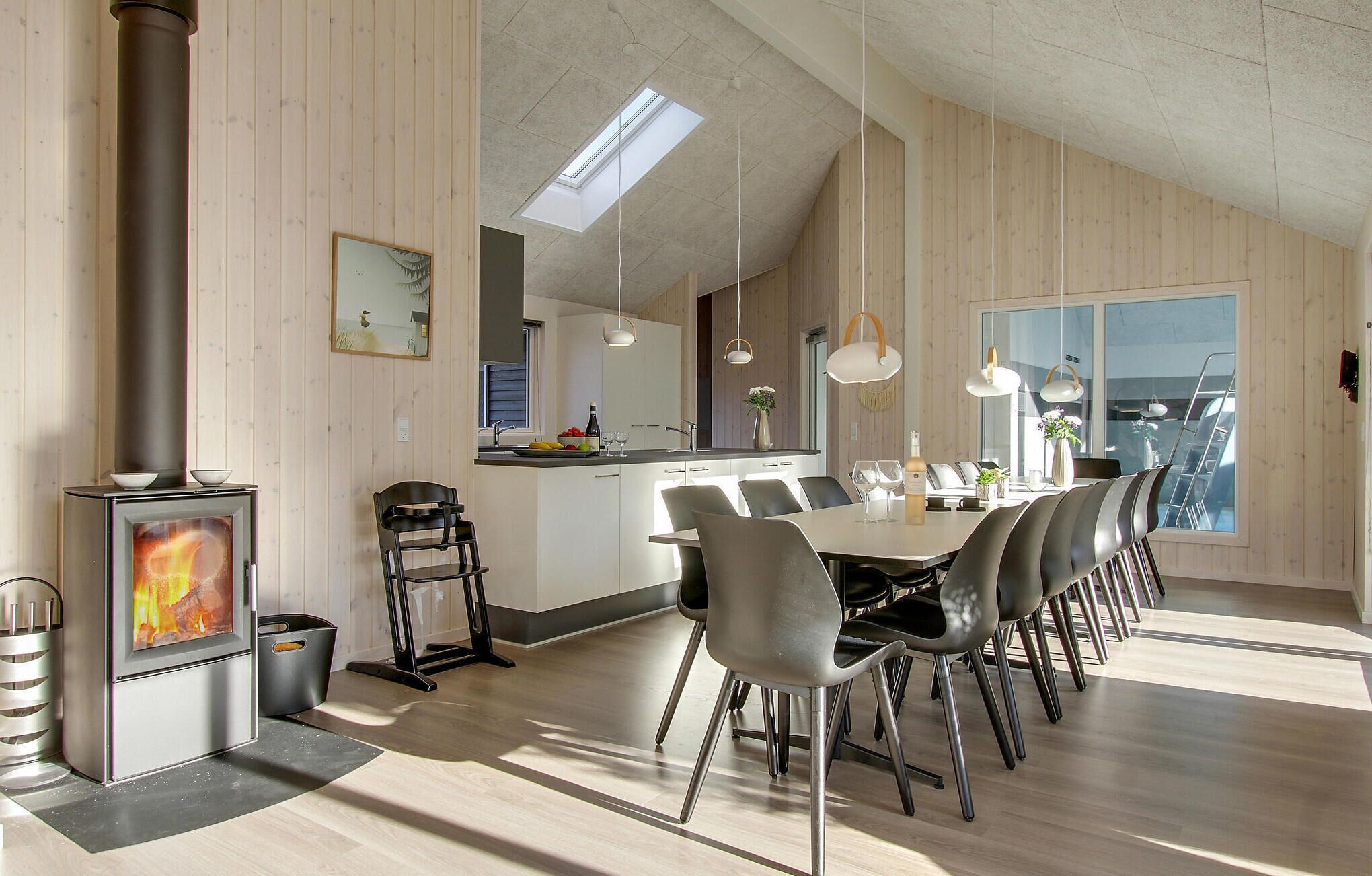 Une cuisine moderne dotée d’un îlot central, d’un coin repas avec une longue table et des chaises, et d’un poêle à bois.
