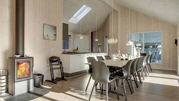 Une cuisine moderne dotée d’un îlot central, d’un coin repas avec une longue table et des chaises, et d’un poêle à bois.