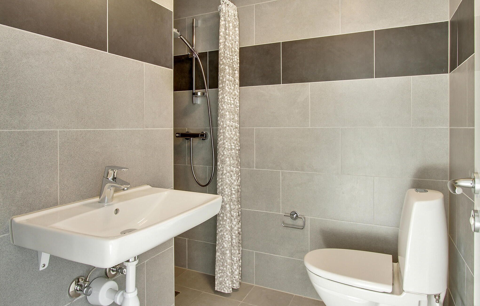 A bathroom with a sink, toilet, shower, and tiled walls.