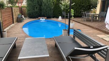 A wooden deck with a swimming pool, lounge chairs, and a table.
