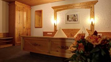 A wooden reception desk with a mirror above it, a framed picture on the wall, and a vase of flowers in the foreground.