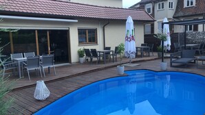 A swimming pool with a wooden deck, outdoor seating, and umbrellas. - Hotel Bruker (Grossbottwar)