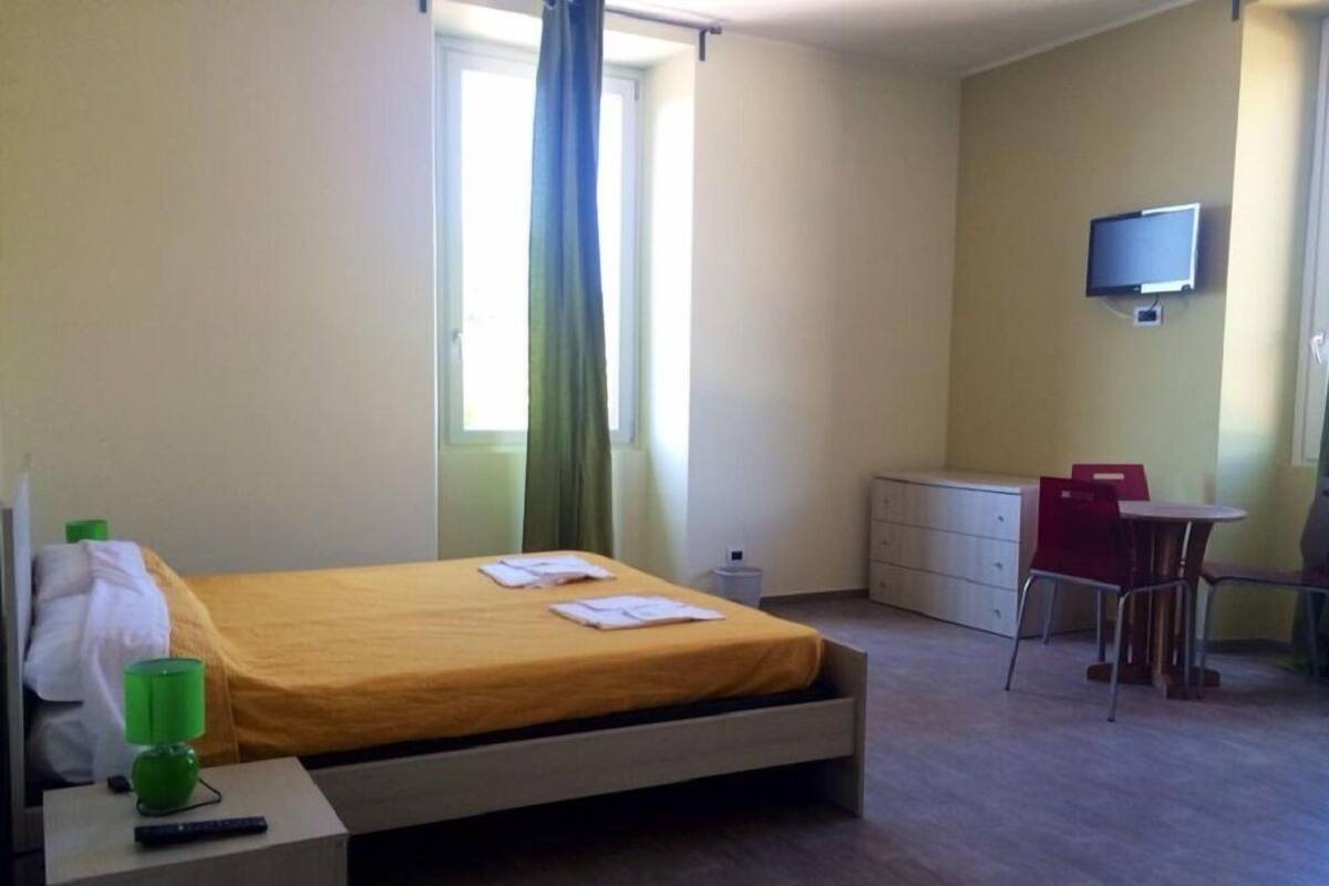 Ein Hotelzimmer mit einem Bett, einem Schreibtisch mit Lampe, einem Sessel, einem Fernseher und einem Fenster mit Vorhängen.