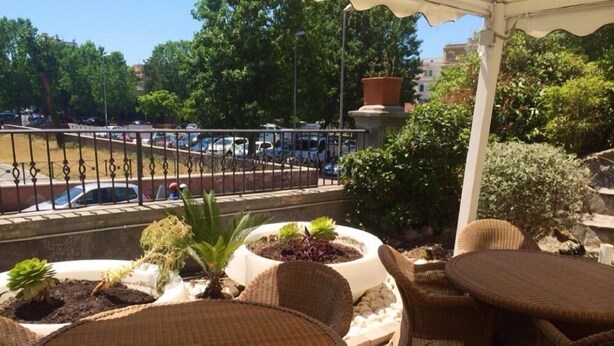 Une terrasse dotée de meubles en osier et agrémentée de plantes en pot, qui offre une vue sur un parking et sur des arbres.