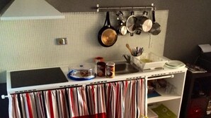 Une cuisine avec un plan de travail blanc, un évier et des casseroles suspendues. On peut voir divers ustensiles de cuisine sur le plan de travail, notamment une tasse verte, une assiette blanche et quelques aliments emballés.