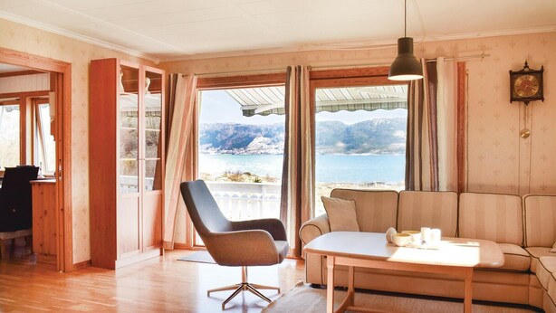 Une pièce avec un plancher en bois, un canapé, une table et une chaise. Il y a une fenêtre qui donne sur des montagnes et un plan d’eau.