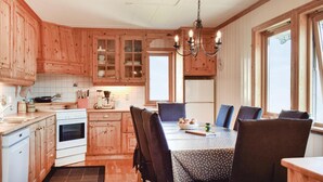 Une cuisine avec des meubles de rangement en bois, une table à manger avec des chaises et un lustre.