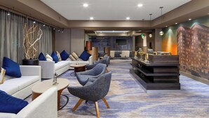 A modern hotel lobby with a reception desk, seating area with sofas and chairs, and a large mural on the wall. - Courtyard by Marriott Dallas Downtown/Reunion District (Dallas)