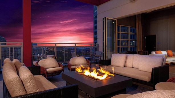 A rooftop lounge with a fire feature, wicker furniture, and a city view at sunset. - Courtyard by Marriott Dallas Downtown/Reunion District (Dallas)