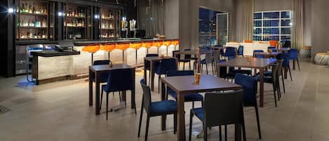 Zona de bar con estantes llenos de botellas de licor, una barra y un área de estar con mesas y sillas.