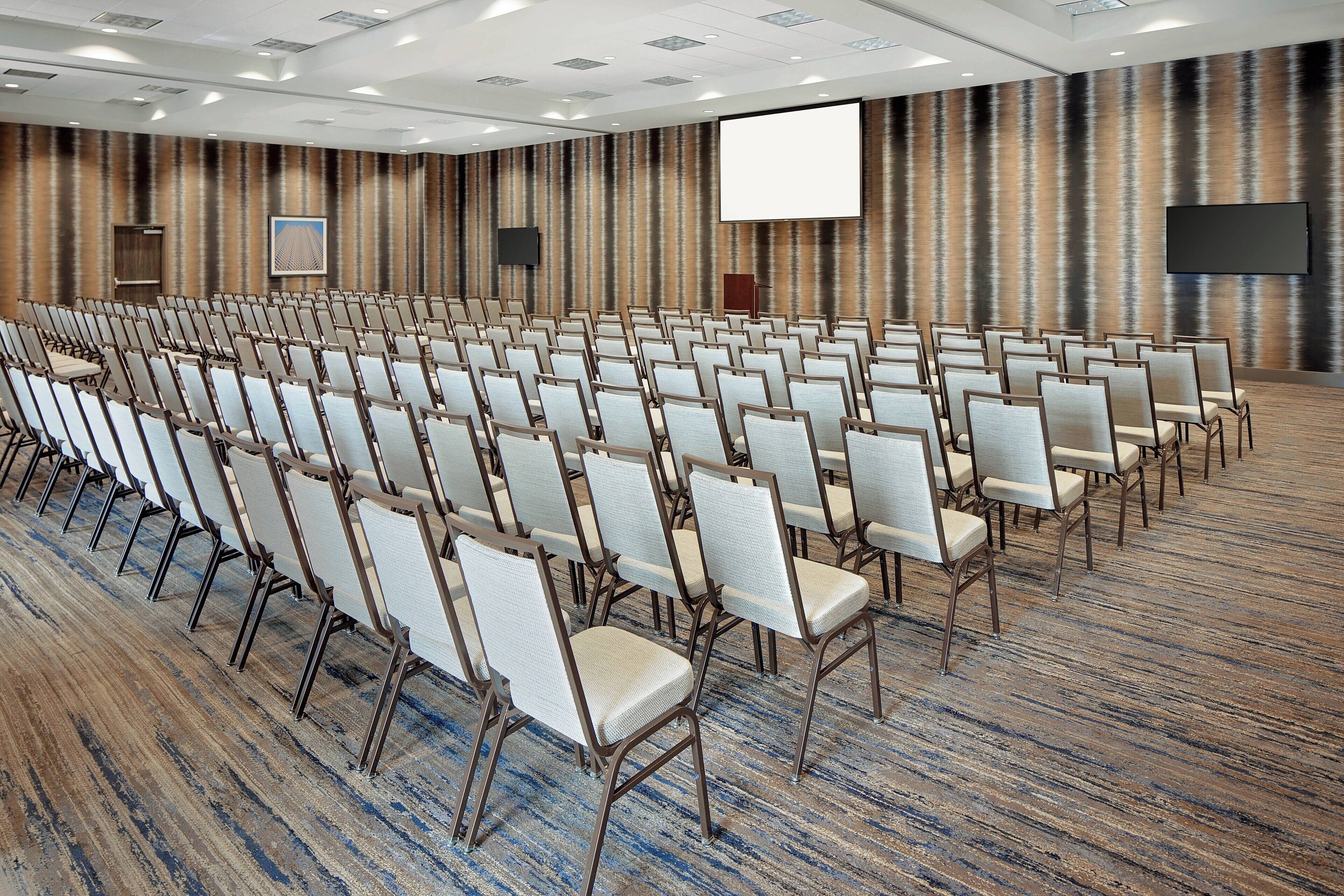 A conference room with rows of chairs, a large screen, and a podium.