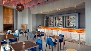 A modern bar area with multiple seating options, including bar stools and tables, and a variety of bottles on shelves. - Courtyard by Marriott Dallas Downtown/Reunion District (Dallas)