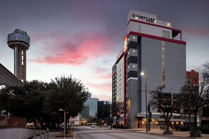 Un hotel con un llamativo letrero de 'Courtyard by Marriott', una alta torre de agua y un moderno horizonte urbano al fondo.