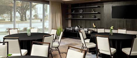 A conference room with a large table, chairs, a TV, and shelves with decorative items.