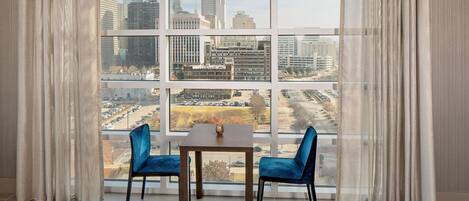 A room with a large window, two blue chairs, and a small table.