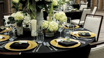 A formal dining table set with gold and black tableware, white flowers, and candles.