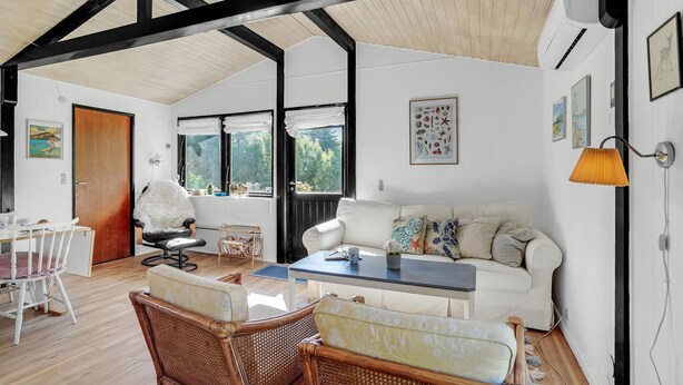 A spacious living area with a high ceiling, a white sofa, a dining table with chairs, and a wicker chair.