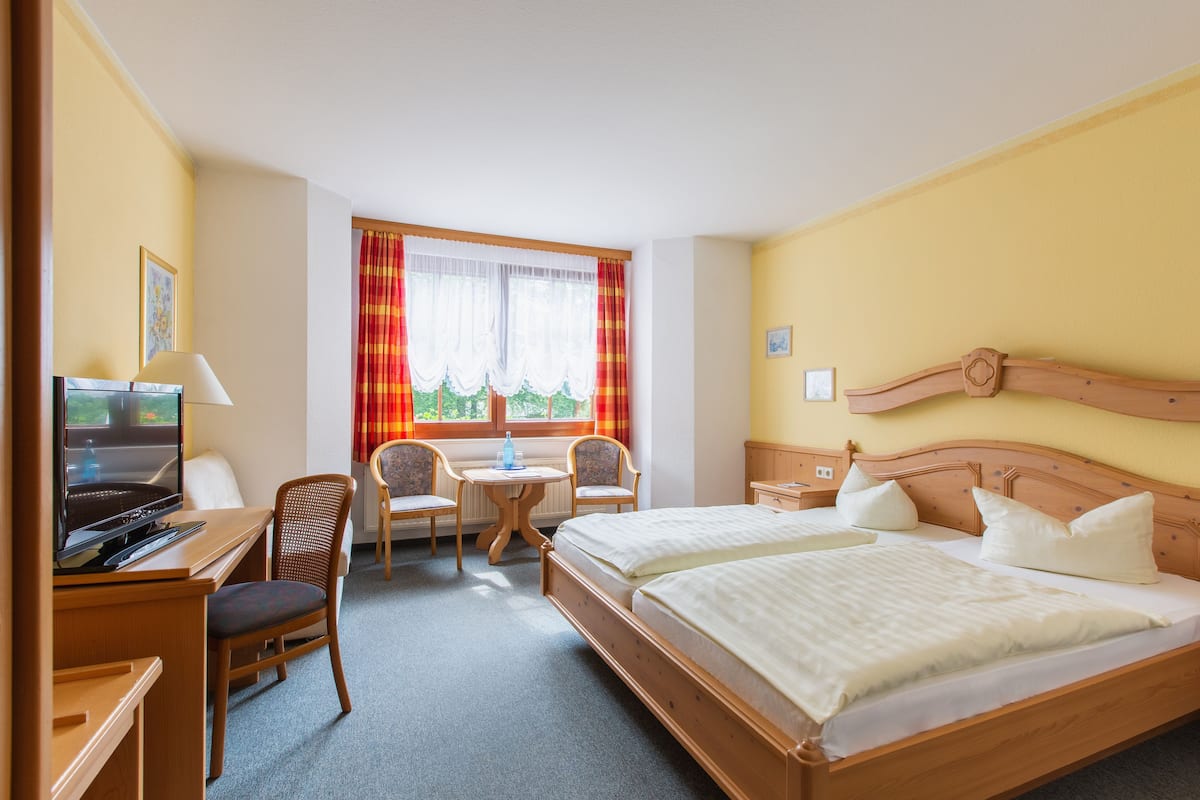Une chambre d’hôtel avec un lit, un bureau avec une télévision, une chaise, une petite table et une fenêtre avec des rideaux.