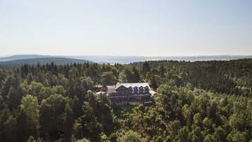 A large, multi-story house surrounded by dense forest, with a clear view of the surrounding landscape.