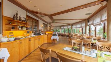 A spacious dining area with wooden tables and chairs, a buffet counter with various food items, and large windows providing natural light.
