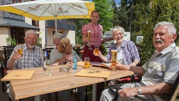 Un grupo de personas sentadas en una mesa al aire libre con bebidas, rodeadas de sombrillas y un edificio de fondo.
