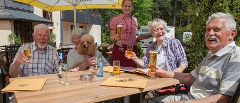 Un grupo de personas sentadas en una mesa al aire libre con bebidas, rodeadas de sombrillas y un edificio de fondo.