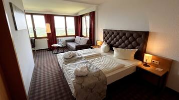 A hotel room with a large bed, a sofa, a small table, and a view of the outdoors.